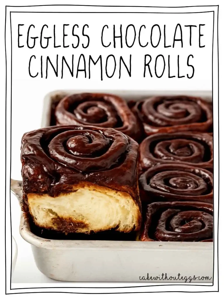 Eggless Chocolate Cinnamon Rolls lifted from a white baking dish, showing its soft, fluffy texture with rich chocolate glaze on top.