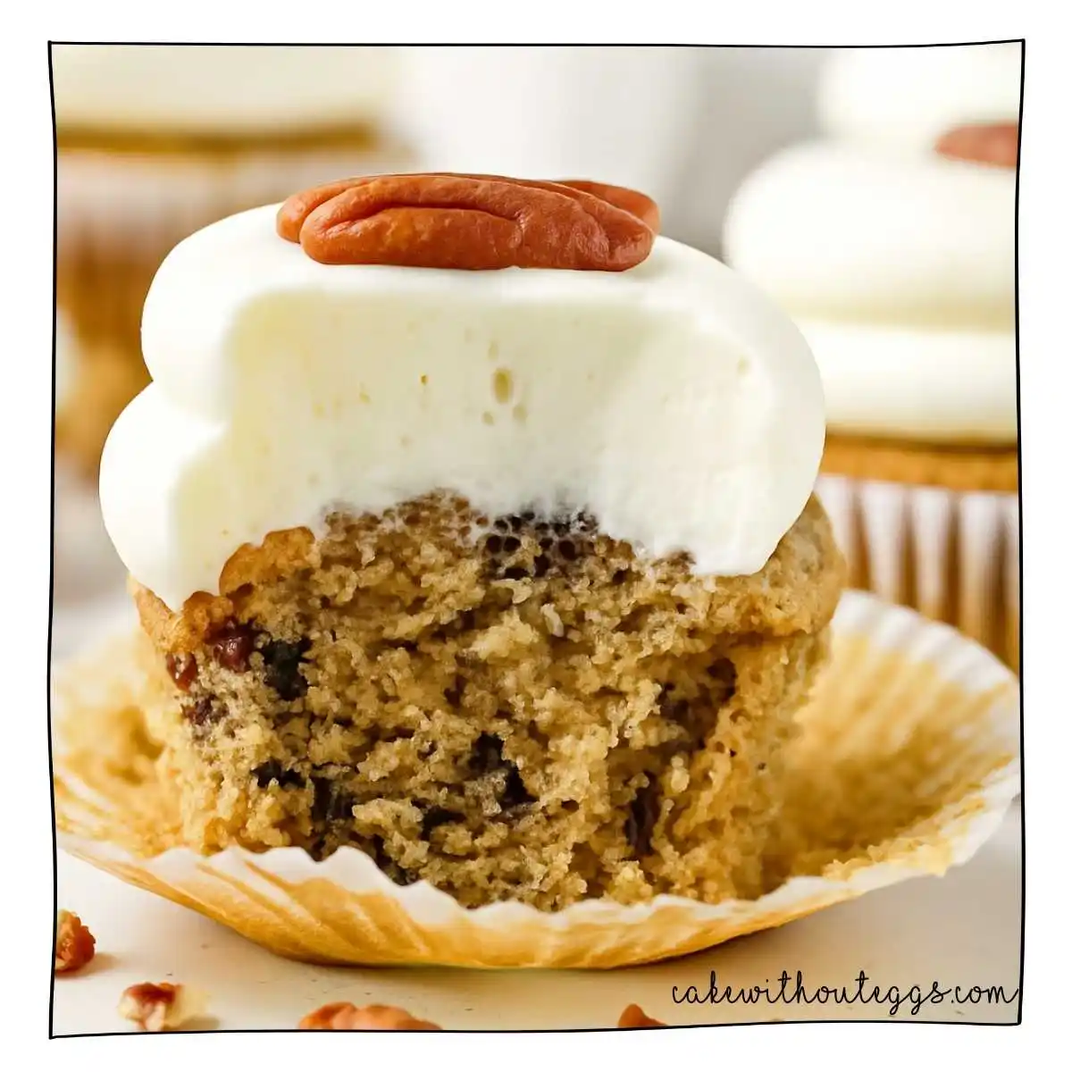 Moist Eggless Hummingbird Cupcake with Cream Cheese Frosting and Pecans Eggless Hummingbird Cupcake with cream cheese frosting and chopped pecans, partially eaten to reveal a moist crumb texture