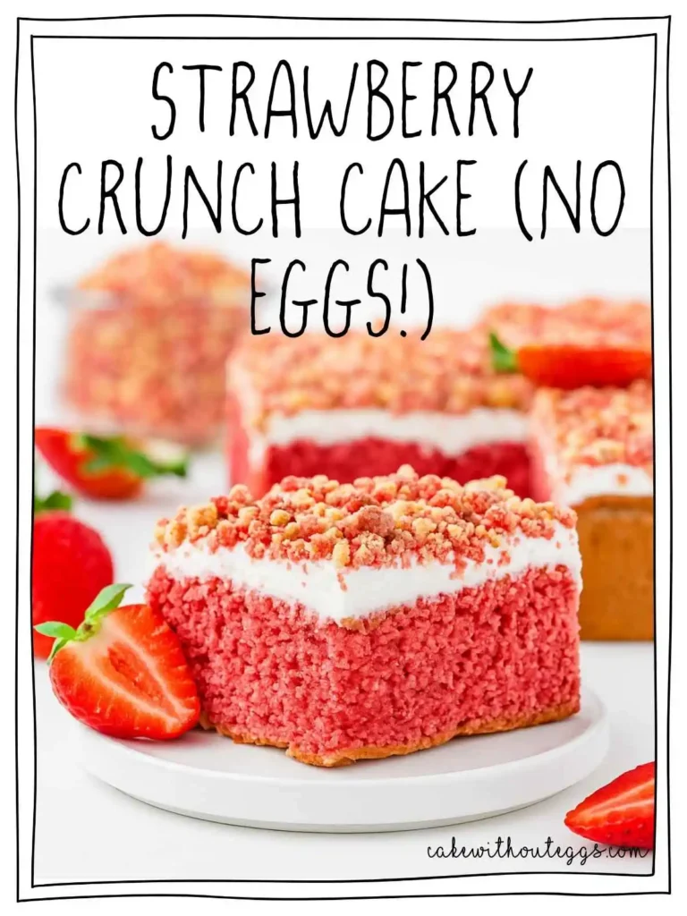 A slice of Eggless Strawberry Crunch Cake topped with creamy white frosting and vibrant strawberry crunch, placed on a white plate with a fresh strawberry garnish, against a white background.