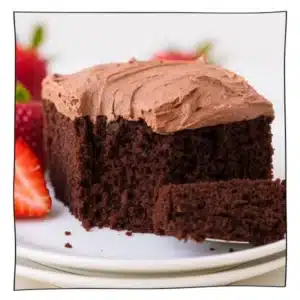 A slice of eggless chocolate cake topped with creamy chocolate frosting, served on a white plate with fresh strawberries